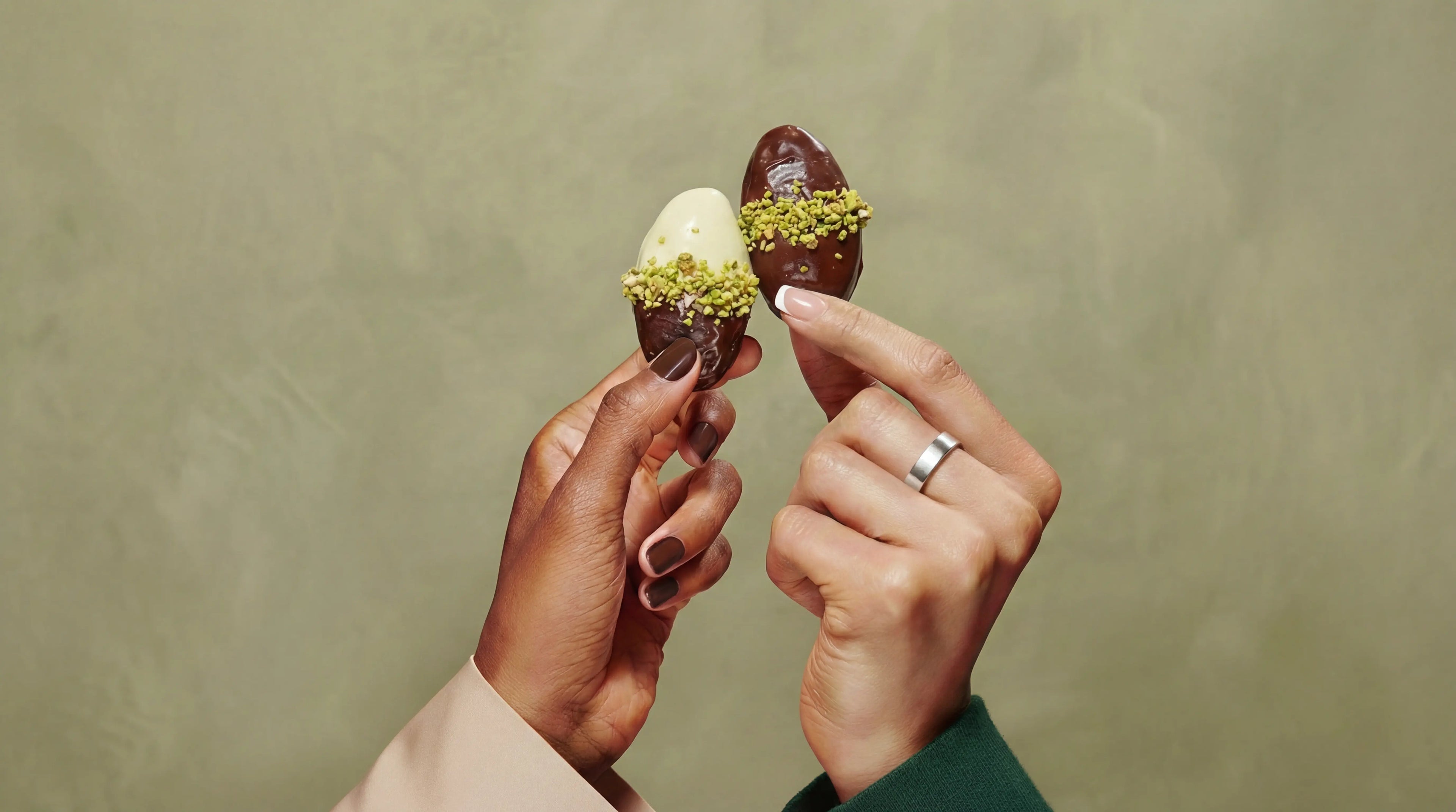 Two hands holding chocolate truffles with pistachio on a plain background